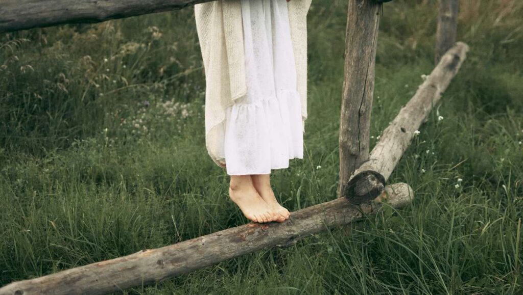 A barefoot Amish girl standing on the fence.