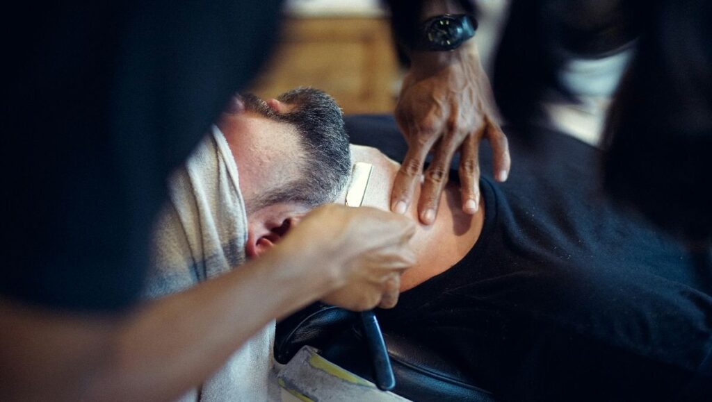 A man shaving client's beard in a salon.