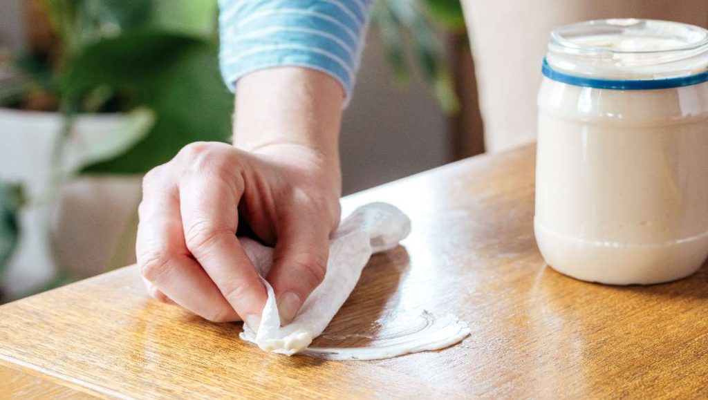 Hand applying mayonnaise to remove water rings in wood