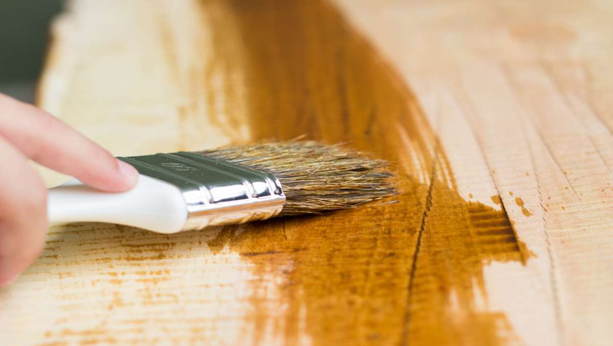 Hand oil varnishing a wooden shelf using paintbrush