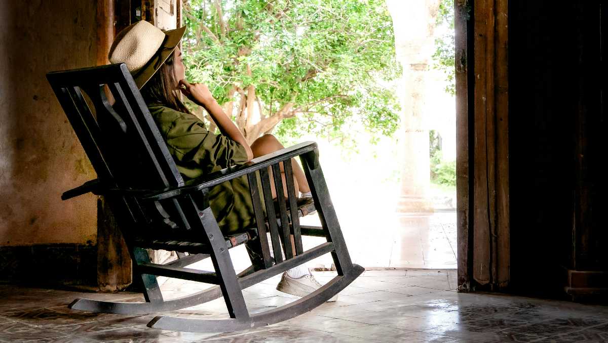 A woman wearing hat sitting on a rocking chair while relaxing and looking outside
